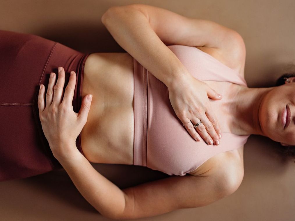 A calm woman rests on a yoga mat in a soft pink top, hands over her chest. This stock image conveys wellness, mindfulness, fitness, relaxation, and focus for yoga or wellness campaigns.